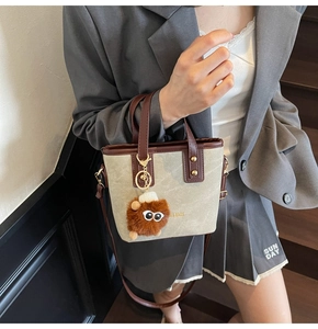 Détail du sac en toile grise avec garniture en cuir brun et breloque peluche sur escalier