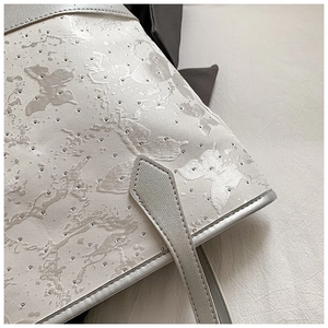 Detail of light gray tote bag featuring butterfly embossed pattern and silver micro-studs