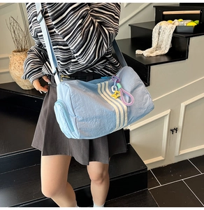 Detail of light blue cylinder nylon crossbody bag featuring white stripes and star charm