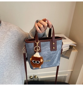 Détail du sac seau en denim bleu avec garniture en cuir brun et breloque en peluche