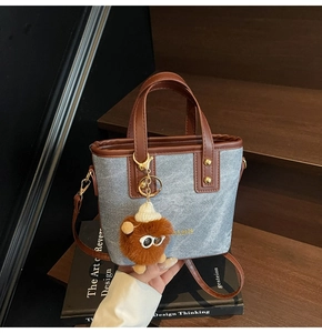 Détail du sac seau en denim bleu et cuir avec un joli pendentif de dessin animé en peluche