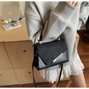 Detail of black crossbody bag with sparkling flap and metal trim on a fashion model