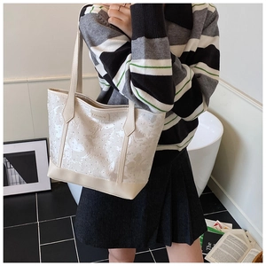 Detail of cream tote bag with butterfly prints and rivets worn by model in casual setting