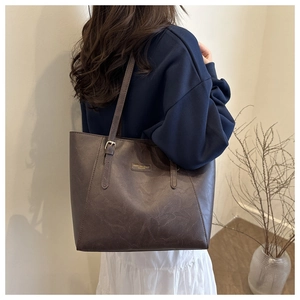 Detail view of deep brown leather tote bag with gold logo on a fashion model