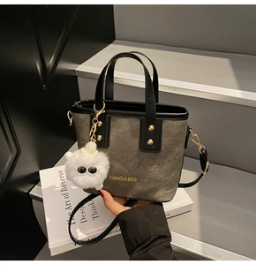 Détail d'un cabas en toile avec anses en cuir noir et charm monstre en peluche blanc