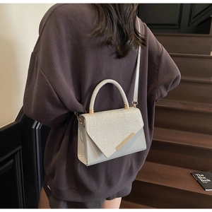 Lifestyle shot of light gray sequined handbag with gold hardware on a shoulder strap