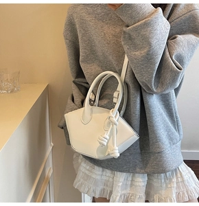 Close-up of white shell bag with knotted handle detail and adjustable shoulder strap