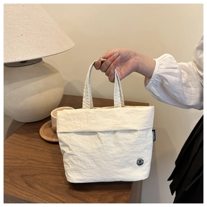 Detalle de mini bolso blanco con textura, etiqueta de marca y logotipo metálico