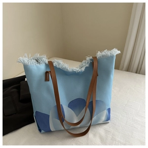 Detalle del bolso tote de lona azul con flecos blancos y asas de cuero marrón