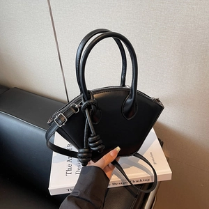Sac à main noir en forme de coquille avec poignées et nœuds décoratifs sur socle épuré
