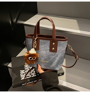 Détail du sac fourre-tout en denim et cuir avec breloque peluche et lettrage doré