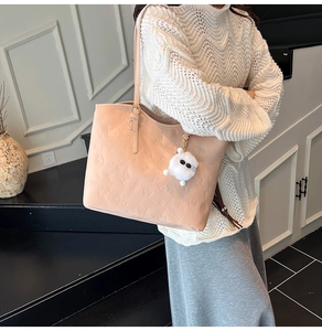 Détail du cabas beige avec gaufrage papillon, texte de mode et breloque pompon en peluche