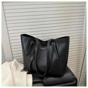 Close-up of black leather tote bag with elegant gold hardware logo on a leather bench