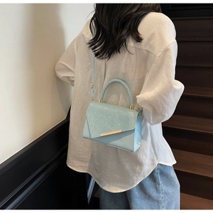 Detail of light blue crossbody bag with glitter finish and gold metal bar accent