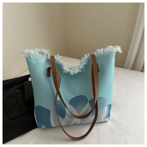 Detalle de bolso tote de lona azul claro con borde de flecos y correa de cuero marrón
