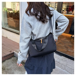 Detailed back side view of the black nylon messenger bag worn by a model in city street