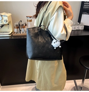 Detail of black PU leather tote with floral embossing and white fuzzy ball charm