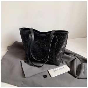 Close-up of black tote bag with textured fabric and stud details on a gray blazer