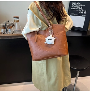Détail d'un cabas en cuir marron foncé avec motifs floraux gaufrés et breloque peluche