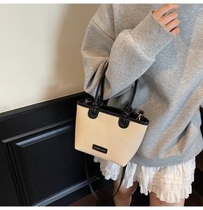 Beige woven tote bag with black trim and handle shown on a model in a minimalist setting