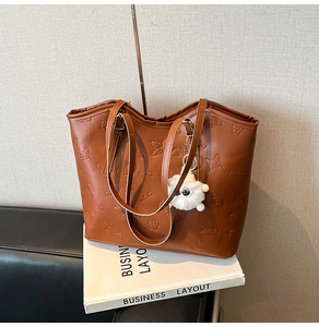 Détail d'un sac cabas en cuir marron avec motifs papillons embossés et pompon en peluche