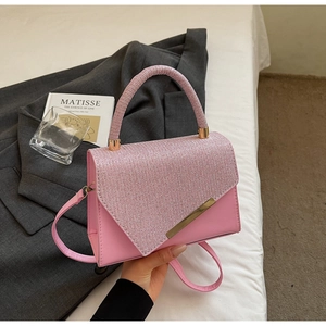 Detailed close-up of pink leather handbag with glittery texture on white fabric backdrop