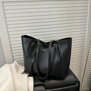 Minimalist black leather tote bag with gold logo and dual adjustable straps for office use