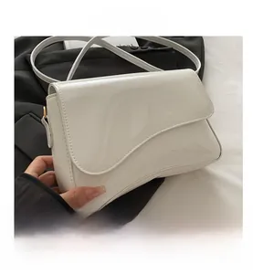 Close-up of white patent leather shoulder bag with irregular wavy flap and thin strap