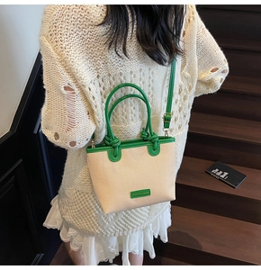 Detail of beige canvas tote bag with green leather trim and adjustable crossbody strap