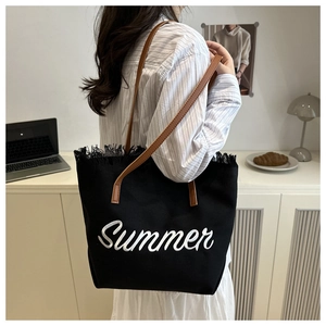 Dettaglio della borsa tote in tela nera con ricamo Summer bianco e bordi con frange