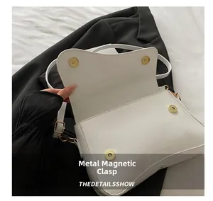 Detail view of white patent leather shoulder bag showing double golden magnetic snap closures