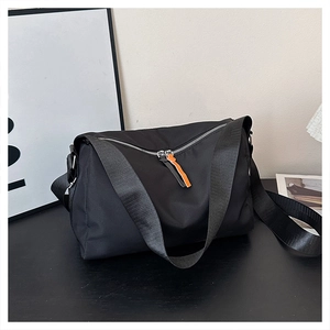 Detail of black crossbody messenger bag with dual zippers and orange strap accent