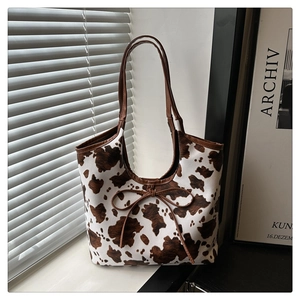 Close-up of cow print tote bag featuring brown ribbon bow and detailed canvas texture