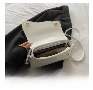 Interior detail of white patent leather shoulder bag showing capacity and gold buckle