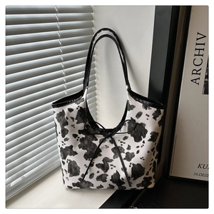 Detail of cow print tote bag featuring a black bow ribbon and long shoulder strap