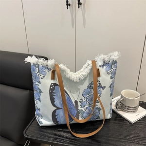 Canvas tote bag with blue butterfly and floral prints, fringe edges and leather handles