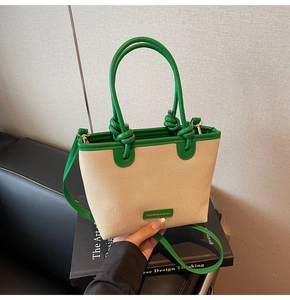 Close-up of woven bucket bag with green leather handles and adjustable shoulder strap