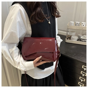 Detail of burgundy glossy patent leather shoulder bag on a model in a stylish indoor setting