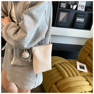 Detail of off-white lychee texture crossbody bag with a chic woven leather ball charm