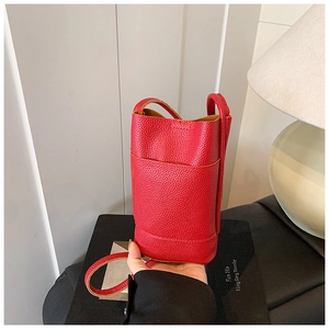 Dettaglio mini borsa a cilindro rossa in pelle a grana su libri di decorazione