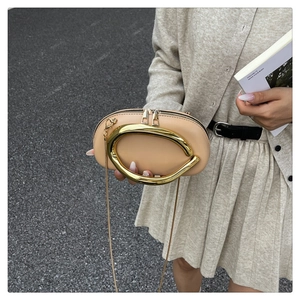 Detail of beige leather bag with large C-shaped gold metal handle and dual zippers