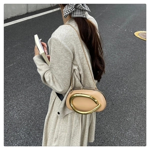 Detail of a chic beige leather crossbody bag with a large gold C-shaped buckle accent