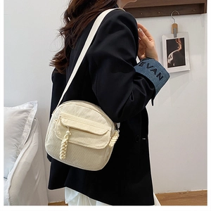 Detail of cream corduroy crossbody bag with woven zipper pull and adjustable strap