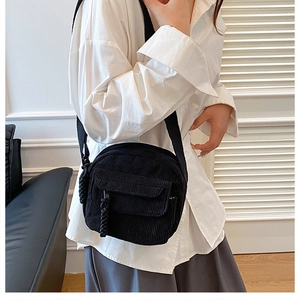 Detail view of black corduroy square crossbody bag with textured fabric and woven charm