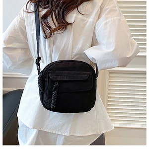 Detail of black corduroy crossbody bag featuring a woven zipper pull and flap front pocket