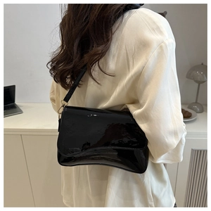 Glossy black patent leather shoulder bag detail shown on model in a modern office setting