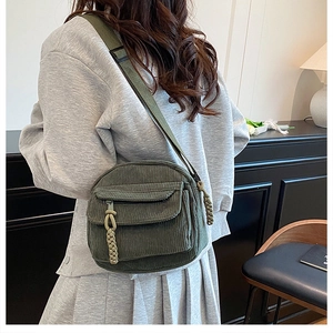 Detail view of a dark green corduroy crossbody bag with woven zipper pull and nylon strap