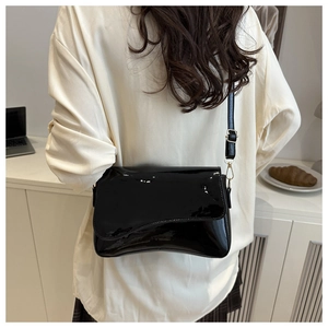 Detail of glossy black patent leather crossbody bag with elegant golden hardware
