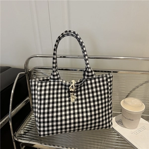 Classic black and white checkered canvas tote bag with woven rope buckle on a metal shelf
