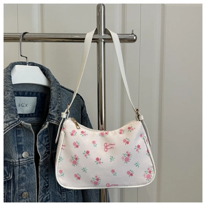 Close-up of a white shoulder bag with pink roses and golden zipper hanging on a denim jacket